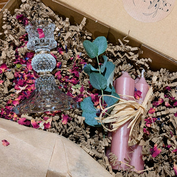 Decorative items including a pressed glass candle holder, pink candles, and rose petals in a gift box 